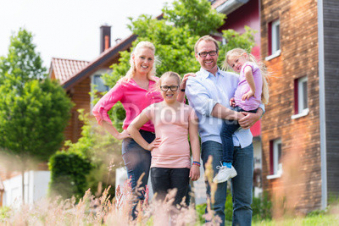 Familie-steht-vor-Haus-oder-Eigenheim-auf-Dorf-Mutter-Vater-und-zwei-Kinder.jpg